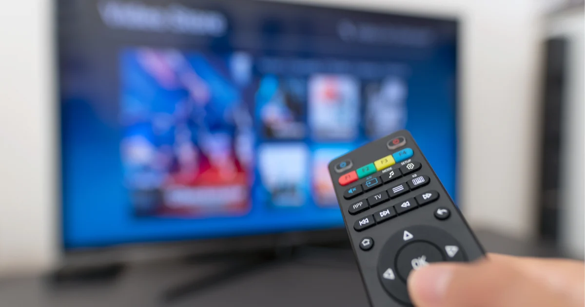 Main tenant une télécommande face à un écran affichant plusieurs applications de streaming